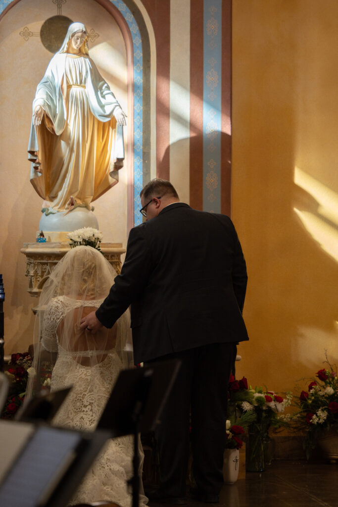 flowers to Mary are tradition during the wedding mass where the newlyweds give flowers to Mary after they receive communion in thanksgiving for her intercession in their relationship, catholic wedding photography by Alexis Dean