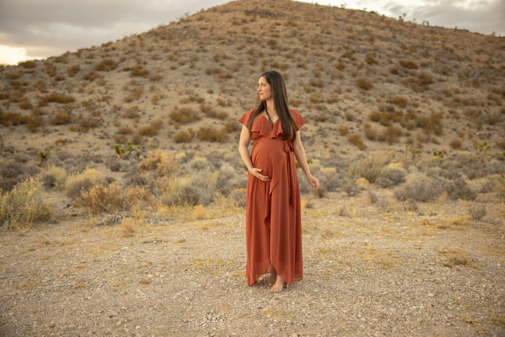 A pregnant mama stands strong in front of mountains near las vegas during a portrait session with Alexis Dean Photography