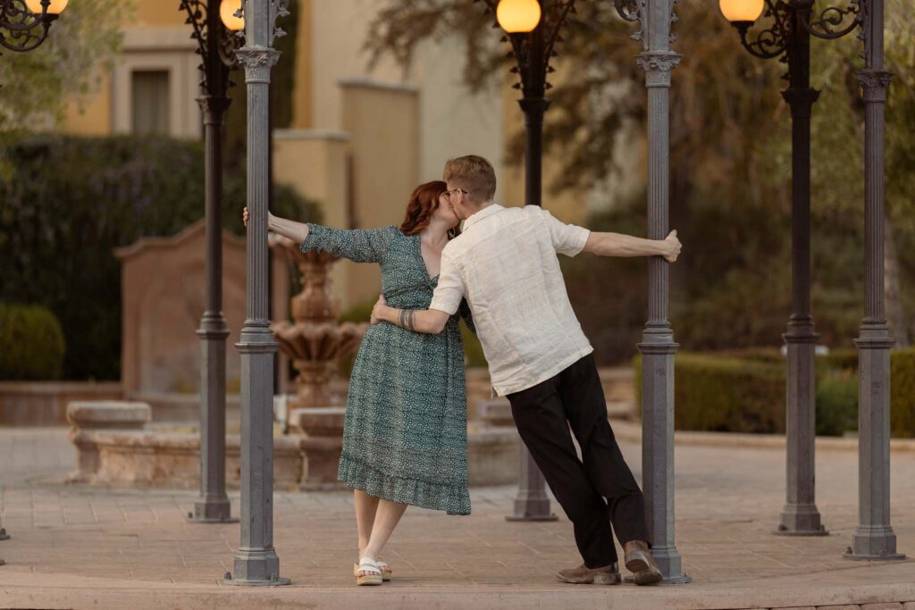 couple holding onto the posts of lake las vegas gazebo while kissing at their couples session with las vegas wedding photographer alexis dean