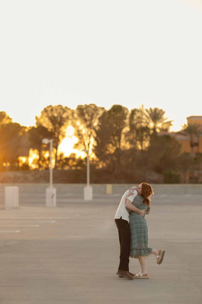 couple hugging on top of parking garage with golden light filtering through the trees in lake las vegas