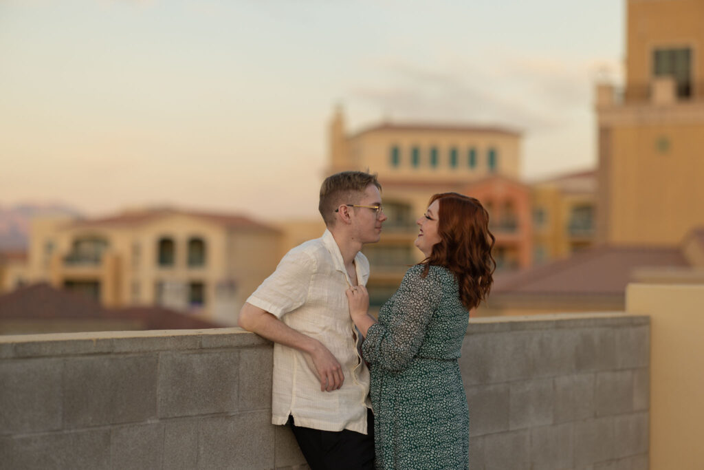 husband and wife leaning against wall at the top of a parking garage overlooking lake las vegas