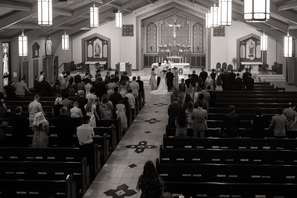 Bride and groom during the Lasso ceremony at Holy Name Catholic Church in Sheridan Colorado from the choir loft by second photographer alexis dean
